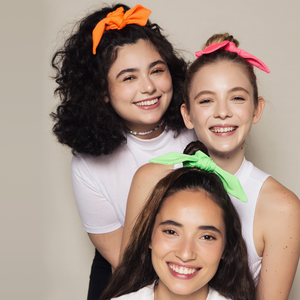 tres meninas sorrindo usando xuxinhas de cabelo colorida