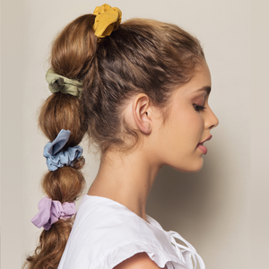 menina loira de lado usando xuxinhas de cabelo scrunchie coloridas